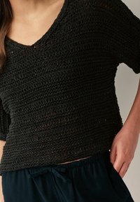 Czarny dzianinowy top charakteryzuje się luźnym krojem, krótkimi rękawami i głębokim dekoltem w serek. Tekstura jest zróżnicowana dzięki poziomym paskom.