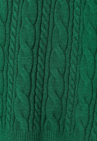 Tessuto lavorato a maglia verde con motivi a cavo verticale e punti torsionati, che mostrano texture e dettagli della maestria nella lavorazione a maglia.