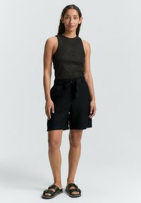 Haut sans manches noir avec un léger éclat, associé à un short noir avec une taille à nouer et des poches latérales, porté avec des sandales noires.