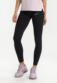 Černé legíny s vysokým pasem, se subtilním logem Nike. Spárované s světle růžovými teniskami s texturovanou tkaninou a viditelným polstrováním.