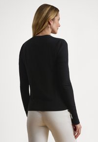 Camisola preta de mangas compridas com decote redondo, textura lisa, design ajustado e bainha canelada, combinada com calças de cor clara.