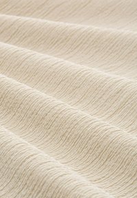 Tessuto crema testurizzato con un motivo ondulato, superficie liscia e una leggera lucentezza, piegato per mostrare variazioni di luce e ombra.