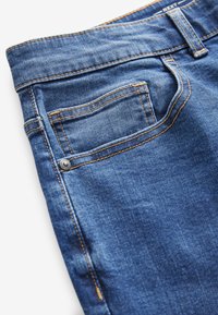 Jeans aus mittlerem Blau mit gelber Naht, einer kleinen Gesäßtasche und einem Knopfdetail. Weiche Textur mit klassischem Design.
