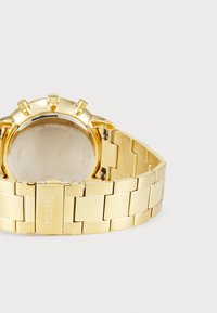 Montre en acier inoxydable doré avec un bracelet chaîné massif, un grand cadran rond avec plusieurs cadrans, et un fermoir à bouton-poussoir à l'arrière.