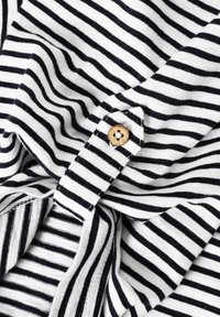 Tissu à rayures horizontales noir et blanc avec un bouton en bois cousu sur une bande rayée, montrant des plis doux et une texture.