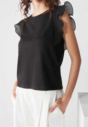 Czarna bluzka z falbankowymi przezroczystymi rękawami, okrągłym dekoltem i luźnym krojem, zestawiona z białymi plisowanymi spodniami. Miękka faktura, casualowy design.