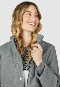 Grau gemischte Wolljacke mit hohem Kragen, Druckknopf- und Reißverschluss, gerippten Bündchen und lockerer Passform, kombiniert mit einem gemusterten Sweater.