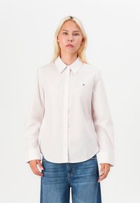 Camicia button-up rosa chiaro con colletto, maniche lunghe e sottili righe verticali; presenta un piccolo logo del marchio sul petto.