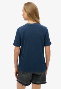 Camiseta de algodón azul marino con cuello redondo, mangas cortas y corte recto, combinada con pantalones cortos de mezclilla negra desgastados.