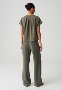 Olive green, short-sleeved top with pleated back, paired with wide-leg pants in matching fabric. Smooth texture and relaxed fit.