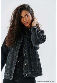 Czarna dżinsowa kurtka o luźnym kroju, z dużymi kieszeniami, zapięciem na guziki i lekko postrzępioną fakturą. Połączona z czarną bluzką.