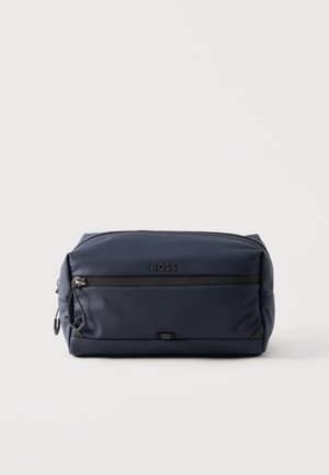 Kompaktowa granatowa kosmetyczka BOSS z przednią kieszenią na suwak i czarnym suwakiem na jednolitym jasnym tle.