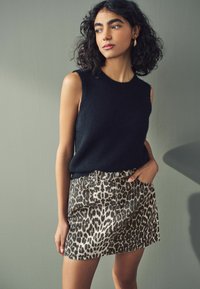 Zwart mouwloos sweater gemaakt van zachte stof, gecombineerd met een denim minirok met luipaardprint, voorzien van een knoopsluiting aan de voorkant en zijzakken.