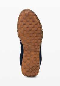 Talpa unei încălțăminte atletice de marina cu o suprafață din cauciuc texturat, având modele pătrate și circulare pentru aderență. Culoare de bej deschis a talpii externe.