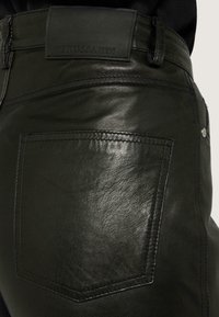 Zelené kožené kalhoty s texturovaným povrchem, obsahující zadní kapsu a embosované logo "TRUSSARDI" na pásku.