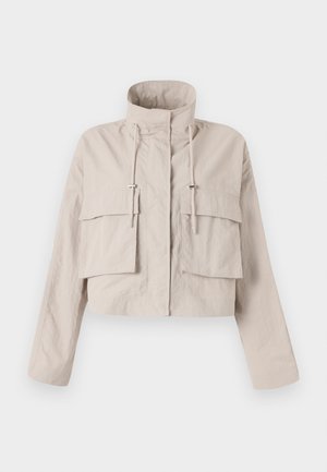 Chaqueta beige corta hecha de una tela liviana, con cuello alzado, cordón ajustable y dos grandes bolsillos con solapa en la parte delantera.