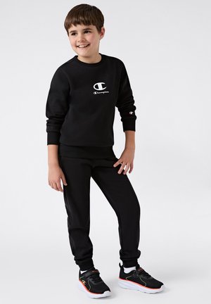 Set di felpa e pantaloni neri, con un logo bianco. Tessuto morbido. Scarpe sportive nere con accenti neon. Outfit casual per lo sport.