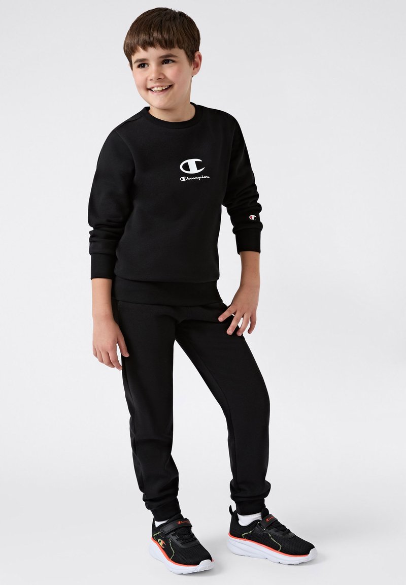 Czarny zestaw bluz i spodni z logo w białym kolorze. Gładka tekstura. Czarne buty sportowe z neonowymi akcentami. Casualowy strój sportowy.