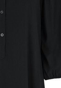Chemise noire à manches longues avec patte boutonnée et poignet élastique sur la manche visible sur fond blanc.