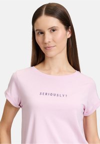 T-shirt en coton rose avec des manches courtes retroussées et un col rond, présentant un texte brodé violet "SÉRIEUSEMENT ?" sur le devant.