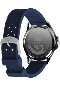 Montre Timex avec un fond en acier inoxydable, bracelet en caoutchouc texturé bleu, boucle en argent gravée du logo Timex et motif de globe gravé.