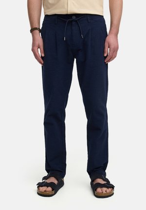 Pantalons bleu marine texturés avec taille à cordon de serrage et plis, associés à des sandales noires avec une semelle en liège.
