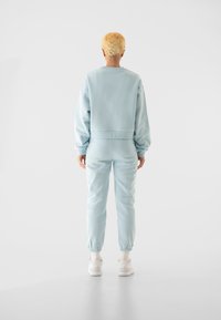 Svetlomodrý skrátený mikina a zodpovedajúce tepláky, vyrobené z mäkkého materiálu s elastickými manžetami a pásom. Biele tenisky dopĺňajú outfit.