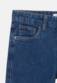 Temno modri kavbojke z klasičnim pet-pocket dizajnom, bakrenimi nitkami in kontrastnim oranžnim šivom ob šivih.