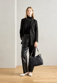 Blazer nero a righe sottili sopra un dolcevita nero, pantaloni in pelle nera, ballerine rosa chiaro e una borsa in pelle nera con dettagli dorati.
