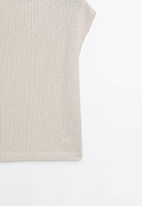 Haut beige en tricot sans manches avec une texture côtelée, présenté sur un fond blanc, mettant l'accent sur la partie supérieure du torse.