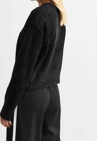 Sweatshirt en polaire noire avec une coupe décontractée, surface texturée et manches longues, associé à un pantalon noir avec une bande latérale blanche.