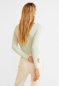 Světle zelený žebrovaný top s dlouhým rukávem a přiléhavým střihem, s výstřihem do V, zkombinovaný se světle barevnými kalhotami volného střihu.