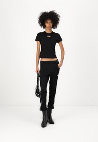 Svart tettsittende t-skjorte med rund hals, kombinert med svarte joggebukser med side-striper. Modellen har på seg svarte ankelstøvler og bærer en veske.