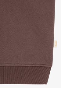Brauner Sweatshirtstoff mit glatter Textur, gerippten Bündchen und einem kleinen Markenschild an der unteren Seite. Einfaches Design, keine Muster oder Akzente.