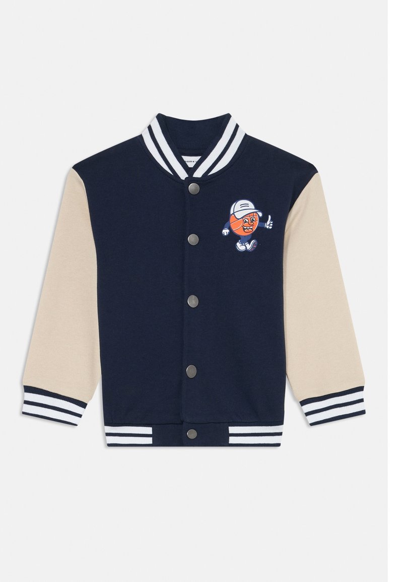 Veste universitaire bleu marine et beige avec col, poignets et ourlet à rayures, ornée d'un personnage de bande dessinée de basketball portant une casquette sur la poitrine.
