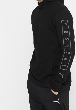 Czarny sweatshirt z wysokim kołnierzem, z szarym nadrukiem "ARSENAL" na jednym rękawie i małym logo Pumy na drugim rękawie. Miękka tkanina.