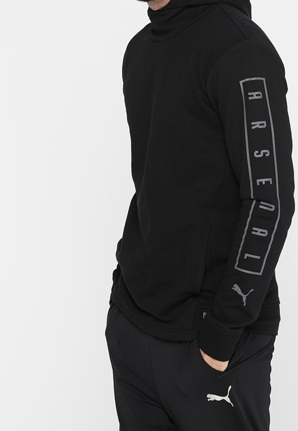 Sudadera negra con cuello alto, que presenta una impresión gris de "ARSENAL" en una manga y un pequeño logo de Puma en la otra manga. Tejido suave.