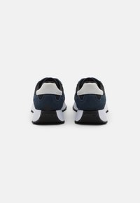 Sneakers in suede nero e blu con dettagli bianchi. Presentano una suola ammortizzata e un tallone posteriore testurizzato, progettati per comfort e supporto.