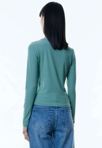 Langmouwtop van groene geribbelde stof met een getailleerde pasvorm, gecombineerd met high-waisted denim jeans met opgestikte zakken.