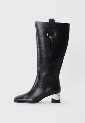 Black leather knee-high boot with a pointed toe, square heel featuring a metallic accent, and a loop detail at the top. Smooth texture.