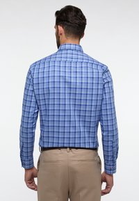 Blauw-wit geruite lange mouwen overhemd met een spread collar en knoopmanchetten. De stof heeft een gladde textuur. Draagt met beige broek.