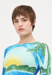 Rash guard med en färgglad tropisk design med blåa, gröna och gula mönster som visar en sol och palmer. Mjuk och elastisk tyg.