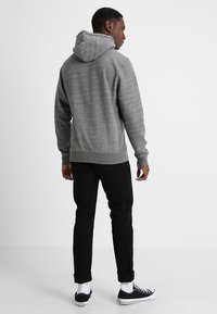 Sudadera gris con una tela texturizada y capucha con cordón, combinada con jeans negros ajustados y zapatillas negras. Diseño sencillo y casual.