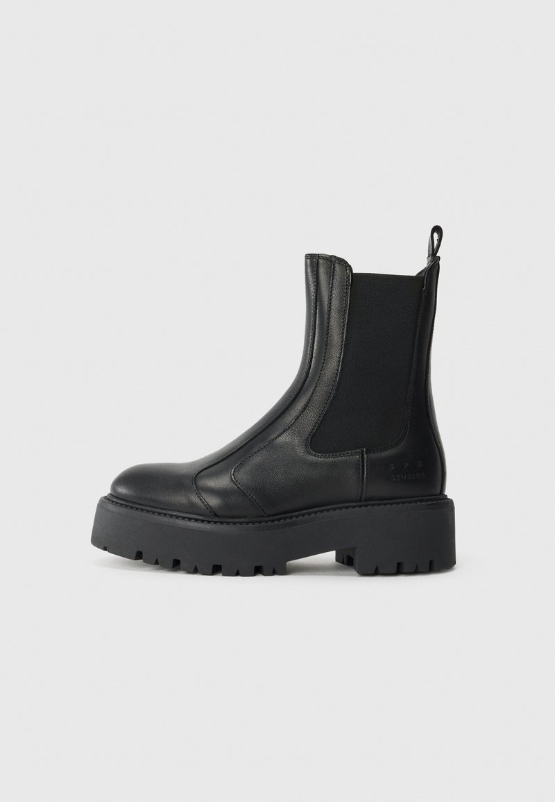 Bottines en cuir noir avec des panneaux élastiques sur les côtés, un bout arrondi et une semelle en caoutchouc texturée épaisse. Comprend une languette à l'arrière.