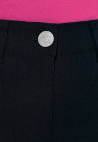 Czarne spodnie z srebrnym metalowym guzikiem na pasku, o gładkiej teksturze i dopasowanym fasonie. Różowa góra widoczna powyżej.