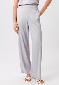 Un pantalon large gris clair en tissu lisse, doté d'une taille élastique et de poches latérales. Assorti à des sandales blanches à lanières.