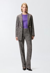 Sivi tvidani odijelo s oblikovanim sakoom i ravnim hlačama. Sako ima zlatne gumbe, nosi se preko ljubičaste majice i s oštrim crnim cipelama.