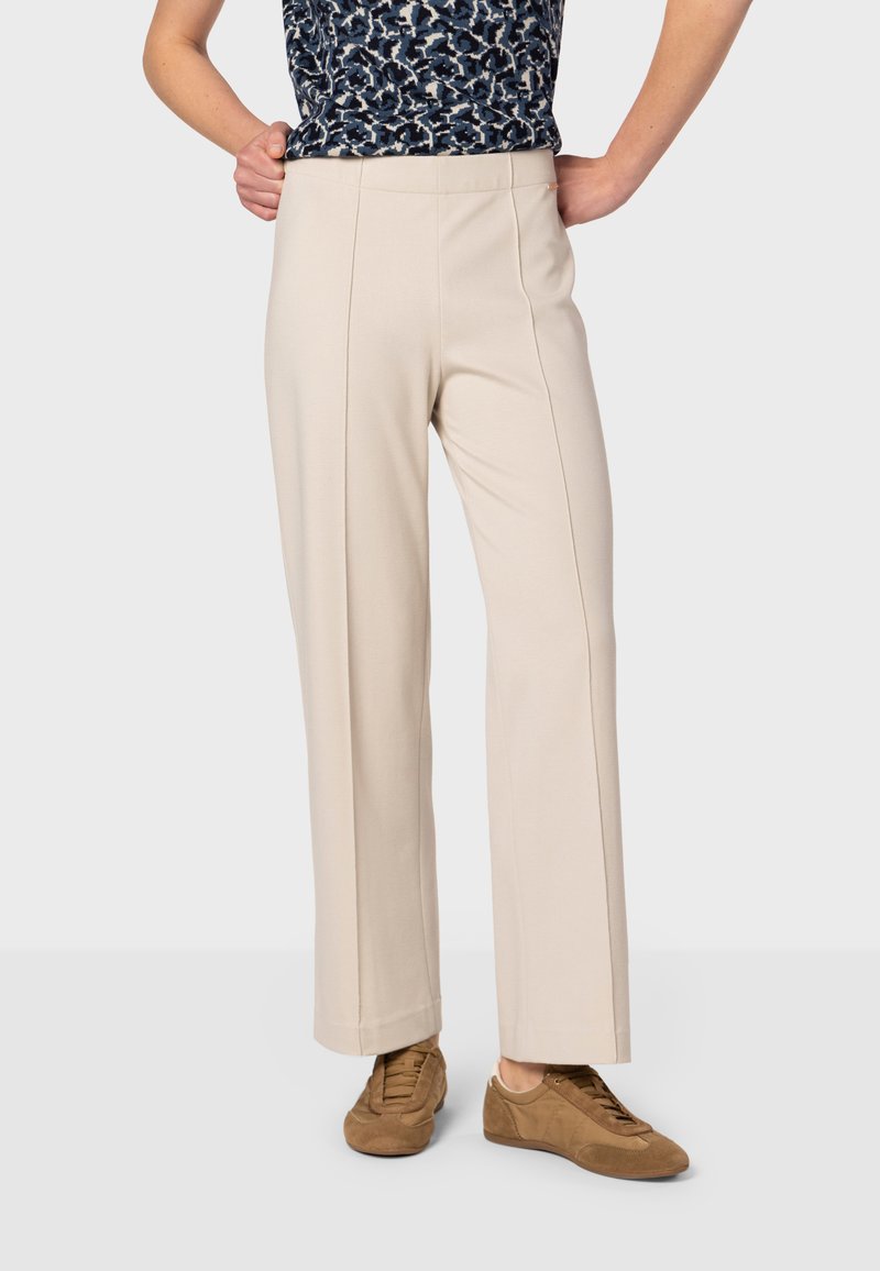 Beige wijde broek met een gladde textuur en een hoge tailleband, voorzien van twee plooien aan de voorkant en gecombineerd met bruine suède sneakers.
