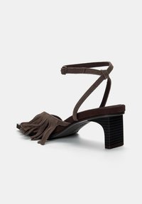 Smeđe suede sandale s potpeticom s detaljem resica na trakom za prste i uskom remenom oko gležnja. Blok potpetica s teksturiranom površinom.