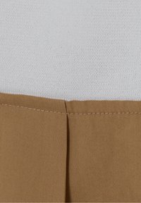 Gros plan sur un tissu tricoté blanc cousu à un tissu tissé marron avec une couture horizontale soignée et un pli vertical dans le tissu marron.